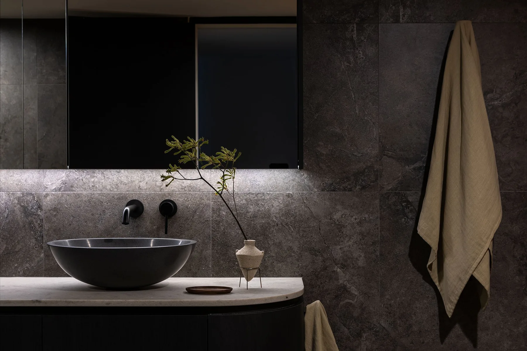 Bathroom with dark stone walls, black vessel basin and curved vanity