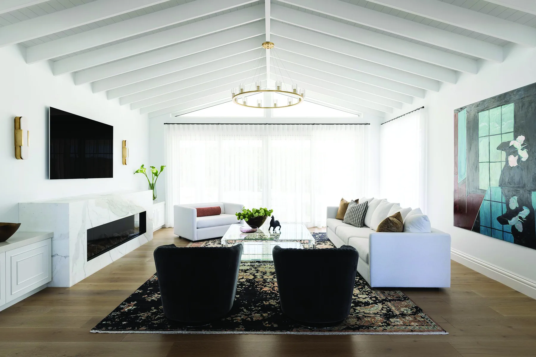 Elanora &mdash; open living room with vaulted white ceiling beams, black armchairs and marble fireplace