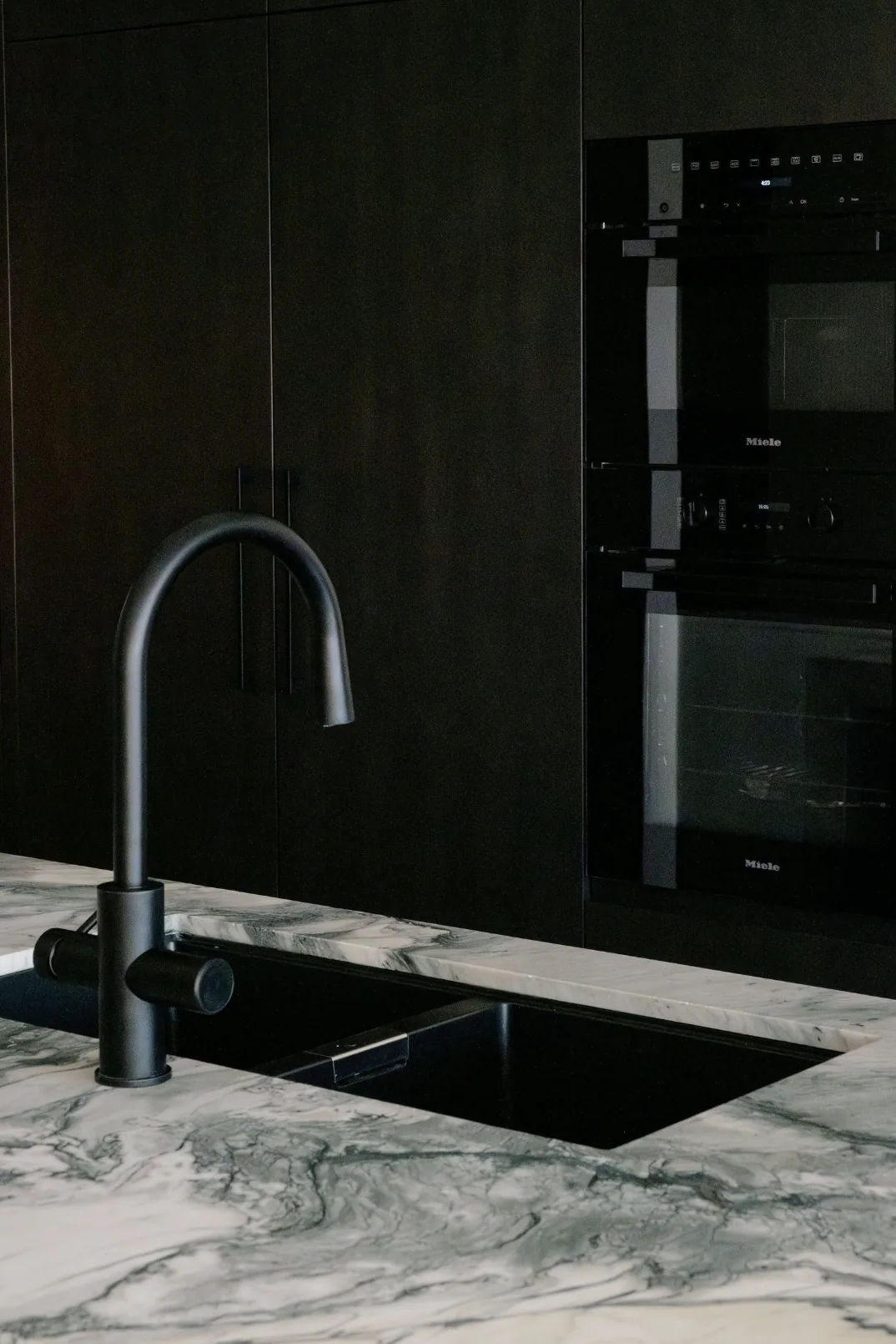 Freshwater &mdash; black tap and sink set into a green-veined marble benchtop with dark oak cabinetry
