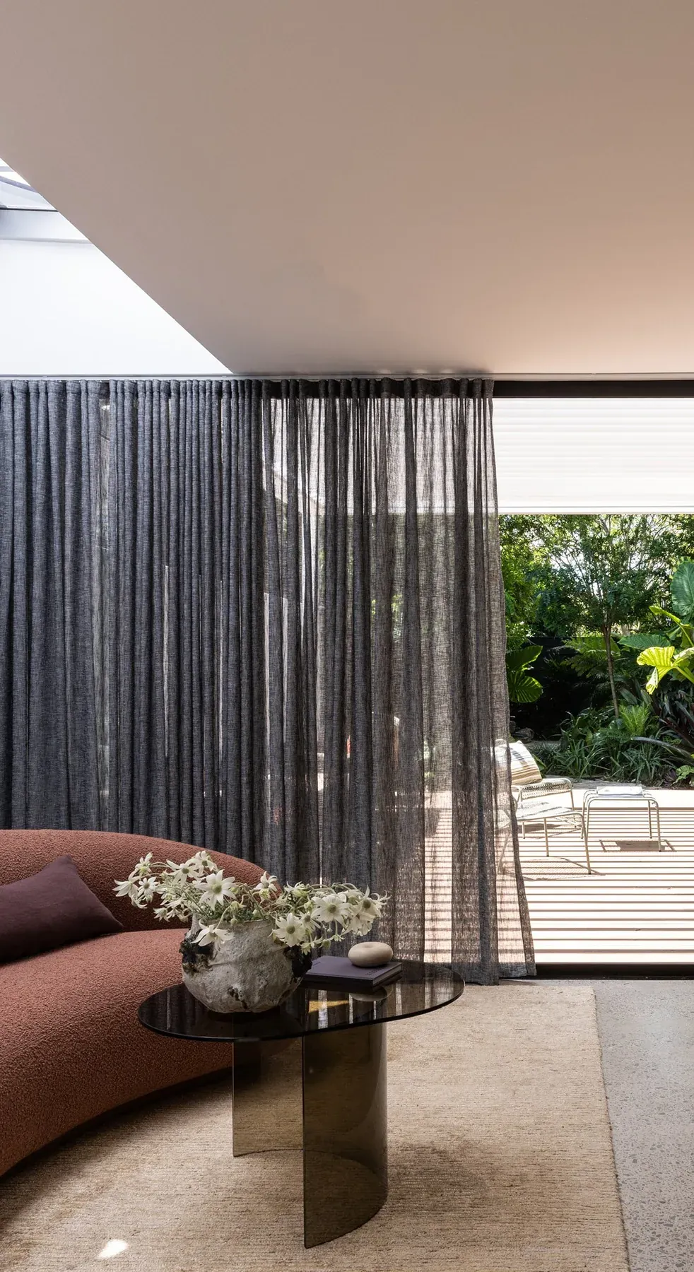 North Sydney &mdash; curved sofa and smoked glass side table beside sheer curtains